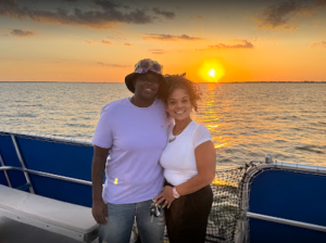 Two people on a boat at sunset, standing close to the railing with water in the background.
